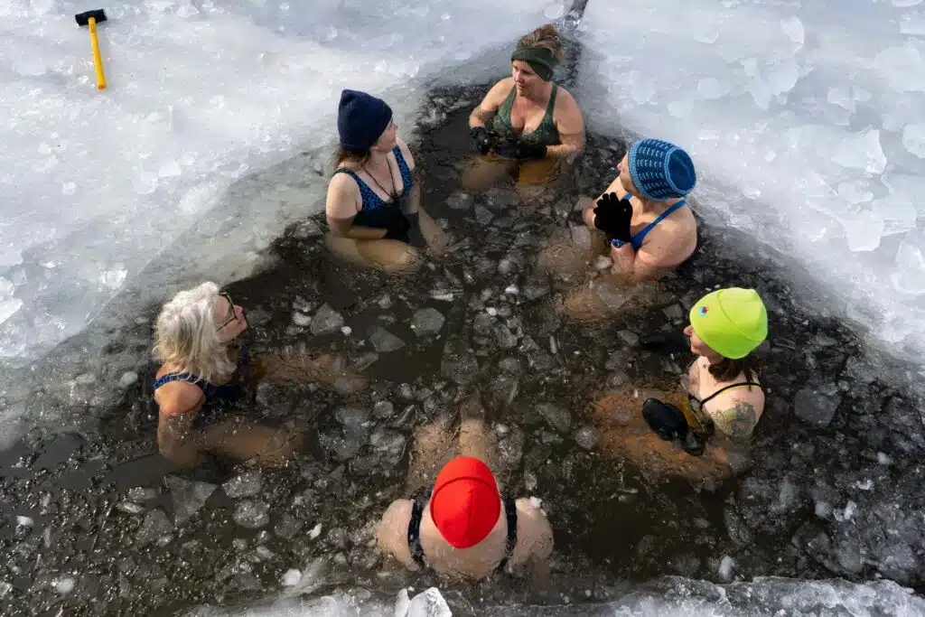 Bain froid dans un trou de glace – les bienfaits du bain froid (élément Eau) Six personnes en bonnet coloré dans un bain froid creusé dans la glace en hiver : les bienfaits du bain froid, élément Eau