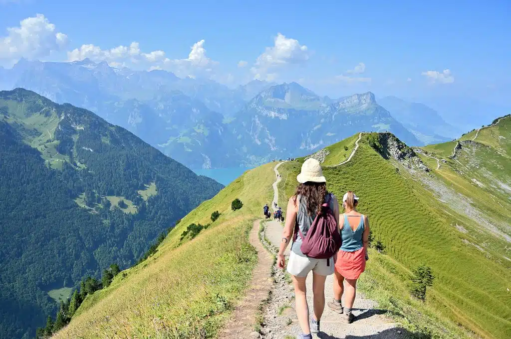 Sentier de crête en montagne – les bienfaits de la randonnée (élément Terre) Trois randonneurs sur un sentier de crête au-dessus d’un lac, en été : les bienfaits de la randonnée en montagne, élément Terre