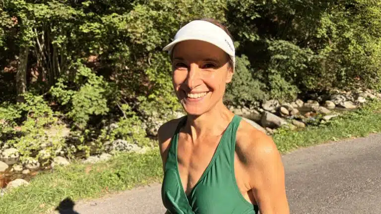 Livre d'Or - Maison Akasha Yoga Femme souriante en maillot de bain vert et visière blanche au bord d'une route longeant une rivière de montagne ensoleillée
