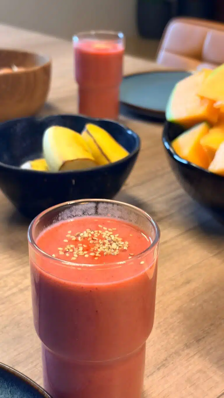 Livre d'Or - Maison Akasha Yoga Gros plan sur un verre de smoothie rouge parsemé de graines de sésame, bananes et melon en arrière-plan sur la table